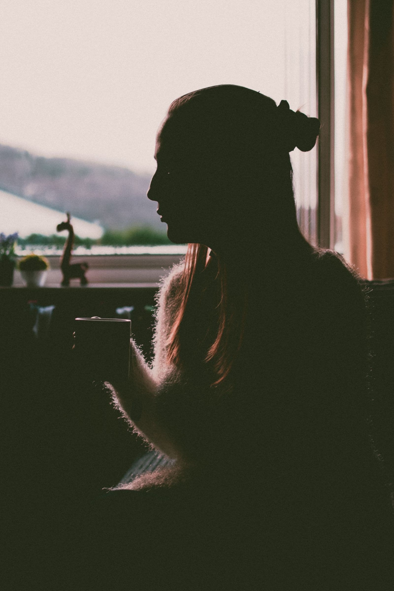 Une personne pensive, une tasse à la main, devant une fenêtre